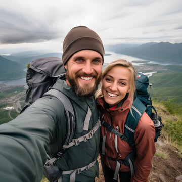 Happy couple of hikers taking selfie picture on top of the mountain - Two travelers with backpack smiling together at camera - Travel blogger influencer streaming using smart mobile phone device, AI