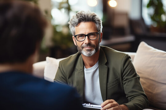 Generative AI illustration of male psychologist talking notes in notebook during therapy session with anonymous patient in office