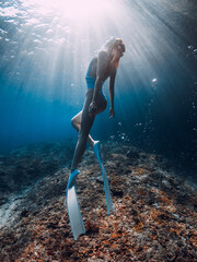 Beautiful woman with fins glide underwater in blue sea. Freediving with sporty girl in ocean and sun rays