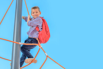 portrait of a joyful child, boy, preschooler, schoolchild with a backpack on the playground against a background of blue sky close-up