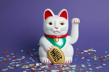 a white Maneki-neko plastic cat, on a confetti carpet