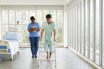 Fototapeta na wymiar Nurse caring male patient with carefully trying walking with walker at hospital. Female assistant taking care male patient with walker. Healthcare and medical concept