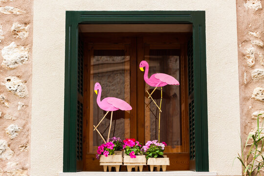 Window with green shutters, decorated with two pink flamingos and some flower pots with pink petunia on "Costitx en Flor" (Costitx in bloom) Flower Fair, Majorca, Spain