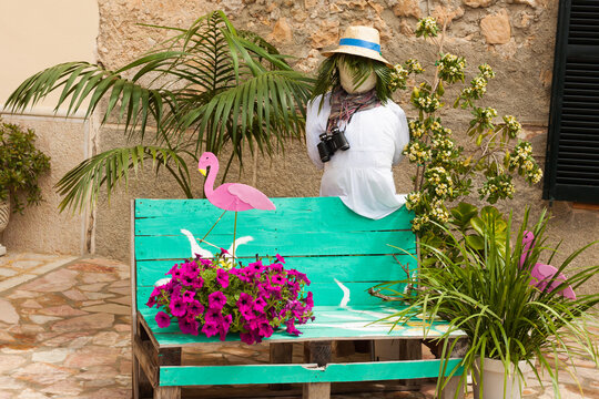 Turquoise bench, decorated with two pink flamingos, a scarecrow with a straw hat and some flower pots, on "Costitx en Flor" (Costitx in bloom) Flower Fair, Majorca, Spain
