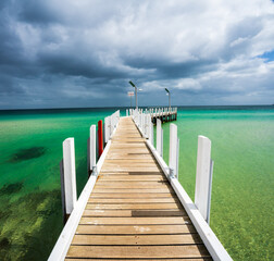 Wooden pier with white posts set in turquoise waters and dramatic sky