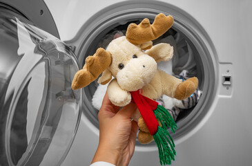A hand puts a soft toy into the washing machine. Cleaning and housekeeping.