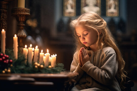 Beautiful Christian child praying over candles in church on Christmas time. Little kid worship with her hands folded. Believer in Christ.