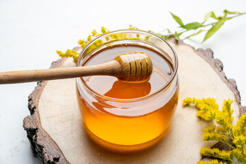 A jar of liquid flower honey, fresh on a cut tree, a light table.