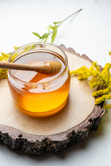 Glass jar with liquid and fresh honey, light background.