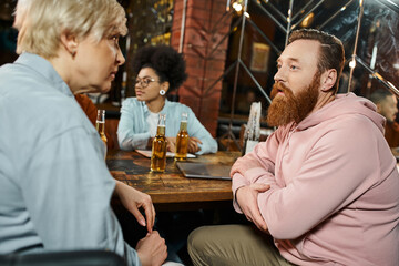 bearded man and middle aged woman talking near african american colleague during meeting in pub