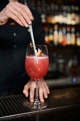 cropped view of bartender adding fresh orange slice in fruit alcohol cocktail on counter in bar