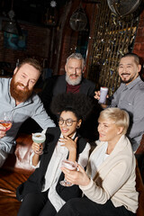 Fototapeta premium overjoyed african american woman laughing near multicultural colleagues with drinks in cocktail bar