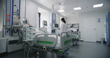Emergency room with modern equipment in hospital. Elderly man in oxygen mask lies and sleeps in bed after successful surgery. Nurse works on computer in intensive care department of medical facility.