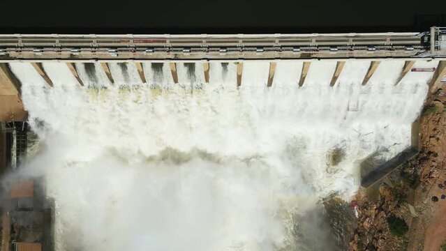Overhead view: white water rushes through open sluice gates of a concrete dam wall
