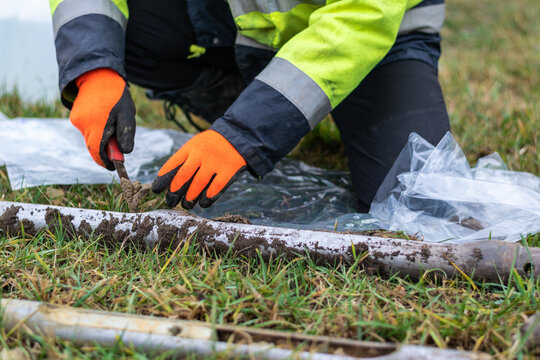 Worker collects soil samples from core drill and putting them to plastic bags, closeup side view