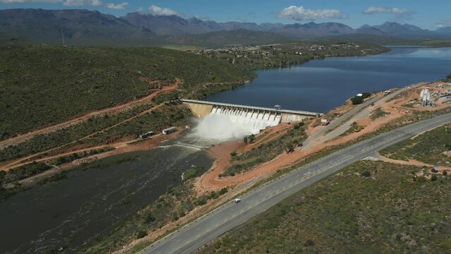 High aerial view panning around Clanwilliam Dam, sluice gates on concrete wall are flowing into Olifants River