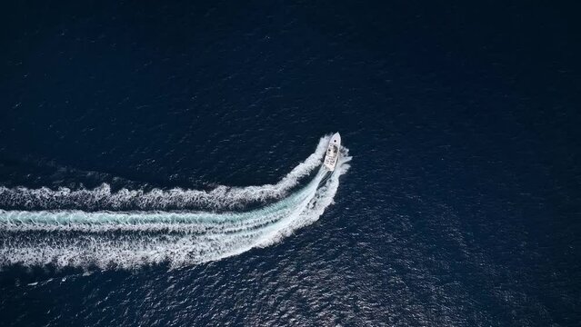 Aerial top view of a motor powerboat forming a circle of waves and bubbles with its engines over the blue sea