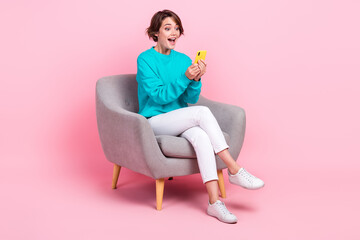 Full length photo of adorable astonished girl influencer sitting chair watching video wifi...