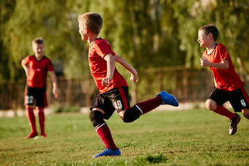 Full length side view portrait of kids, football players in sport uniform training, running at speed in motion before match on soccer field on sunny summer day.