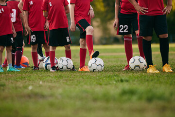Cropped photo of little soccer players wearing sport uniform in jersey, shorts and cleats with a lot of balls. Kids play football on field. Football school.