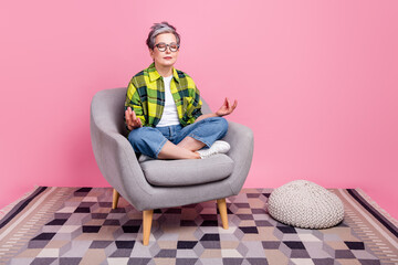 Full length photo of peaceful elderly woman wear checkered shirt sit on armchair in meditation pose...