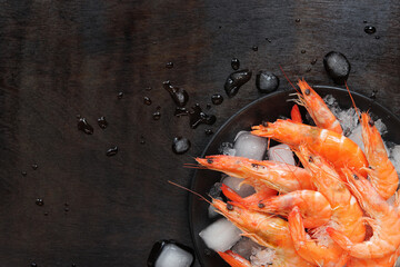 Fresh chilled shrimp in a plate with ice on a dark wooden background. Boiled shrimp in a black plate with ice, top view. Seafood on crushed ice. Healthy eating concept