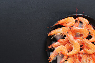 Chilled shrimp in a plate with ice on a dark background. Boiled shrimp in a black plate with ice, top view. Seafood on crushed ice. Healthy eating concept