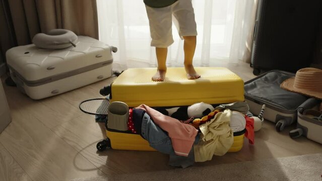 Legs of baby enthusiastically jumping on packed suitcase, charging whole room with exciting energy before travel trip. Child in anticipation of unforgettable vacation holiday happily jumps on suitcase
