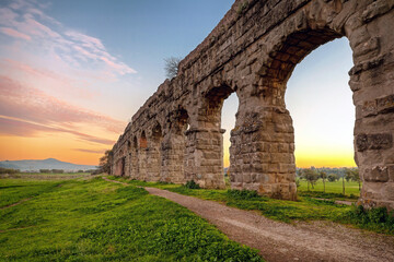 Roman aqueduct. Arches of an ancient Roman aqueduct, made of blocks of tufa. A path runs along the property in a green park in the outskirts of Rome.