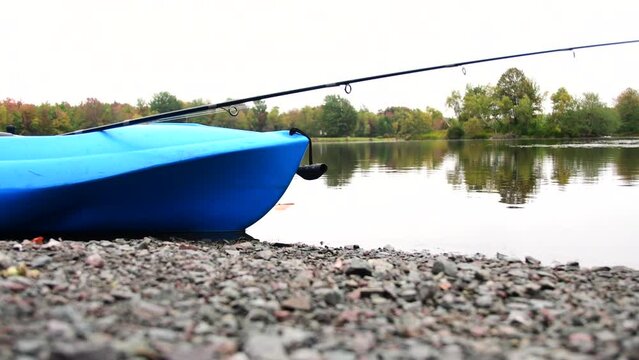 Kayak with fishing rod on lake shore, ready for fishing adventure, hobbies leisure activities, overcast fall season day.