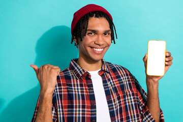 Photo of optimistic guy cornrows checkered shirt hold smartphone indicating at eshop empty space isolated on teal color background