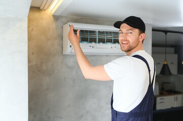 Smiling young male electrician repair conditioner in client home. Man mechanic or repairman fix filters in air condition device at customer house