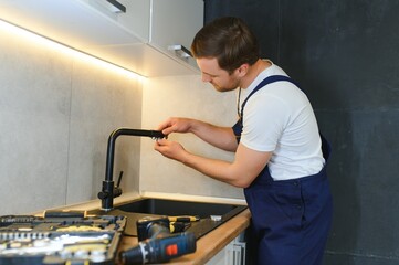 Young Repairman Installing Faucet Of Kitchen Sink In Kitchen Room