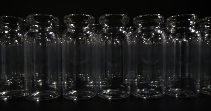 Empty glass vials for vaccination lined up on black surface in dark room. Concept of medical and laboratory glassware in black studio