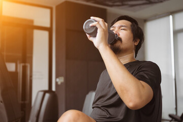 Tired male is drinking water while working out in gym. Healthy man is doing cardio exercise on...