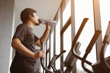 Tired male is drinking water while working out in gym. Healthy man is exercising cardio on...