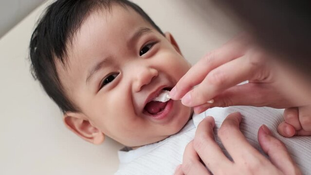 Cleaning Asian baby's mouth. Mom helps to brush the teeth. Baby care, baby's first teeth. Embracing the Concept of Baby Care.