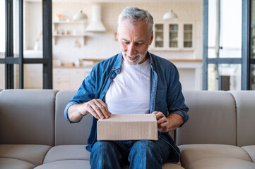 Smiling satisfied mature man unpacking expected parcel from internet shop