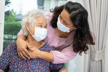 Caregiver help Asian senior woman on wheelchair and wearing a face mask for protect safety...