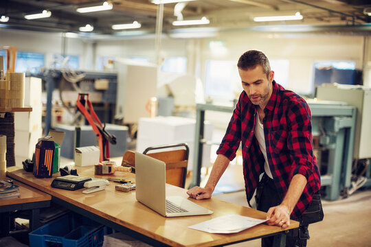 Middle aged Caucasian man working on a laptop in a printing press office