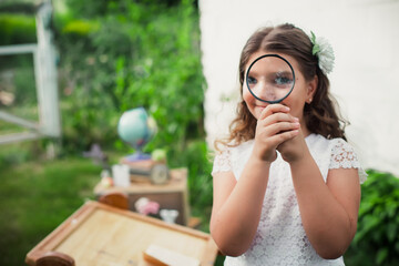 Happy Primary Girl holds and studies nature with a magnifying glass. Learning outside for the prevention of colds. Walfdorf School. Eco-friendly learning. Creative concept with Back to school theme