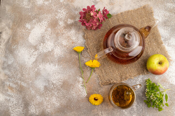 Red tea with herbs in glass teapot on brown concrete. Top view, copy space.