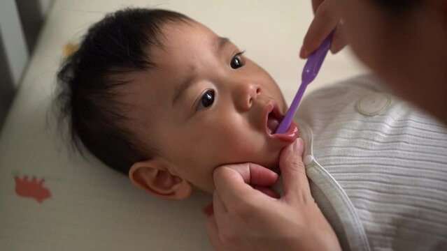 Cleaning Asian baby's mouth. Mom helps to brush the teeth. Baby care, baby's first teeth. Embracing the Concept of Baby Care.