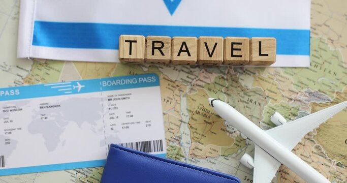 Word Travel made of wooden Latin cubes on world map near toy airplane and flight tickets. Concept of world travelling against Israel flag