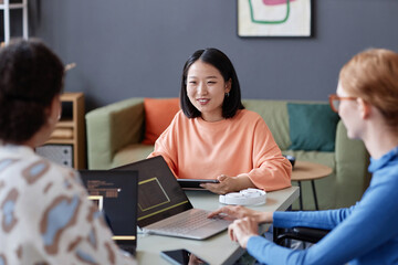 Portrait of smiling young Asian woman leading meeting with IT department in office