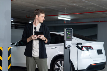 Young man travel with EV electric car to shopping center parking lot charging in downtown city...