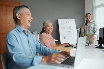 Fototapeta premium Senior couple having fun in computer class, they are typing and joking around