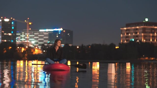 Young woman on a stand up paddle board sup on a lake during floating lantern lights festival at night 