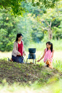 Vertical image of Asian woman look like mother prepare to cook rice with bonfire near rice field and her daughter sit beside.