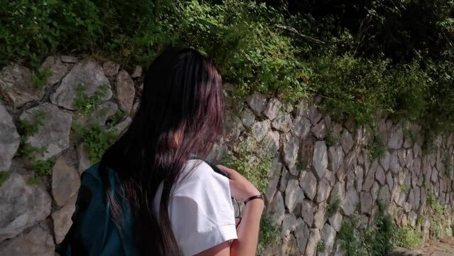 A tourist with a backpack on her shoulder walking down some steps next to an old stone wall in the city of Gaeta